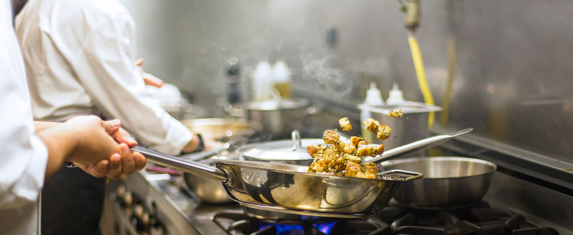 Köche stehen in einer Küche und bereiten auf einem Gasherd Essen zu.