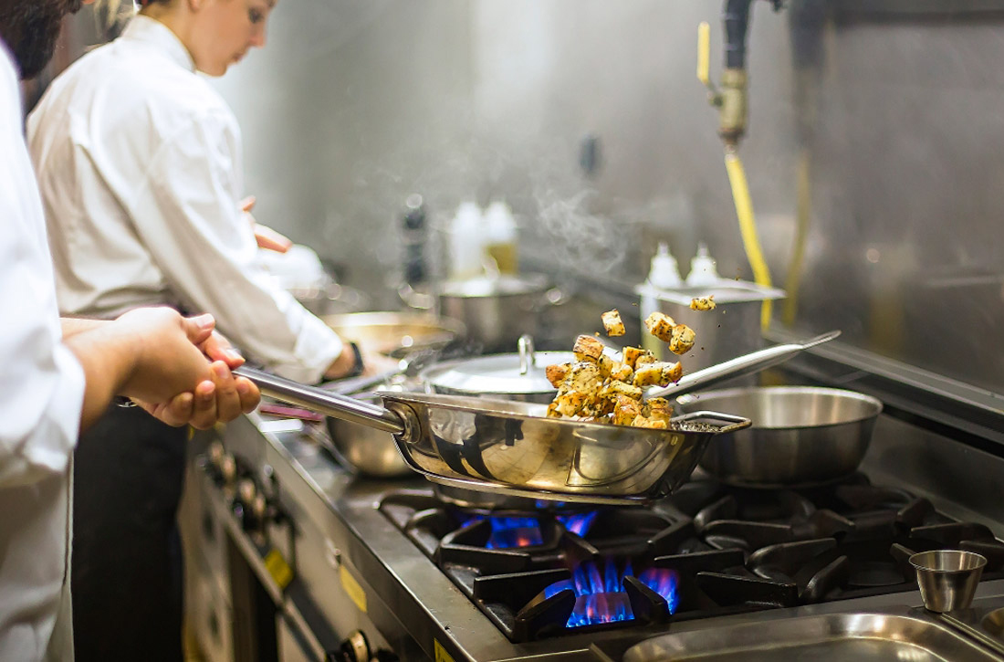 Köche bereiten in einer Küche Essen auf einem Gasherd zu.