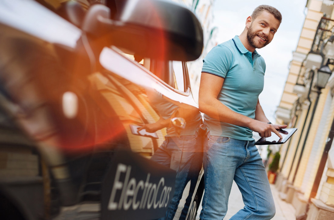 Ein Mann lehnt an einem Elektroauto und schaut auf sein Tablet.