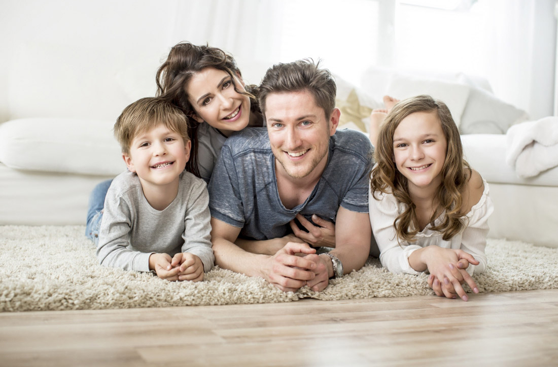 Eltern liegen mit Tochter und Sohn im Wohnzimmer auf dem Teppich.