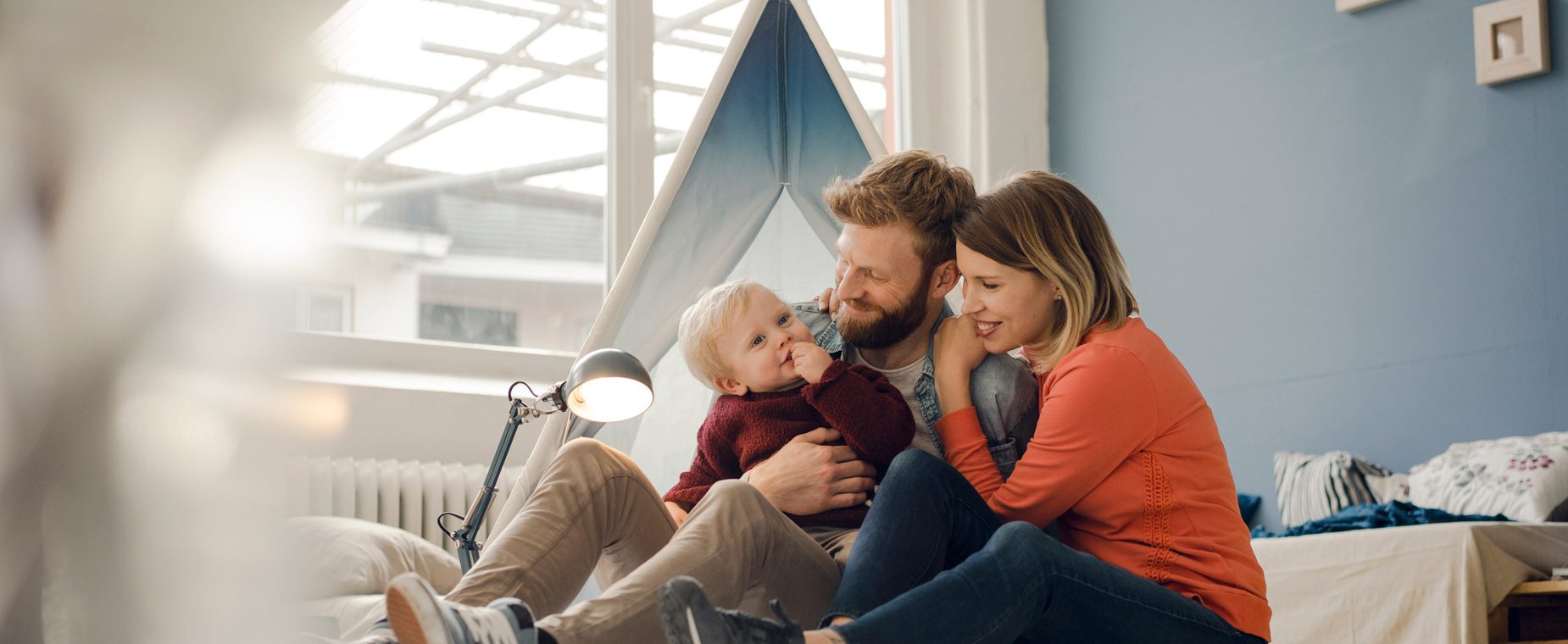 Eltern sitzen mit ihrem Kleinkind im erleuchteten Kinderzimmer. 