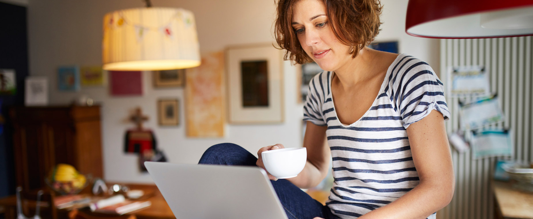 Eine Frau sitzt im Esszimmer und schaut auf ihr Notebook.