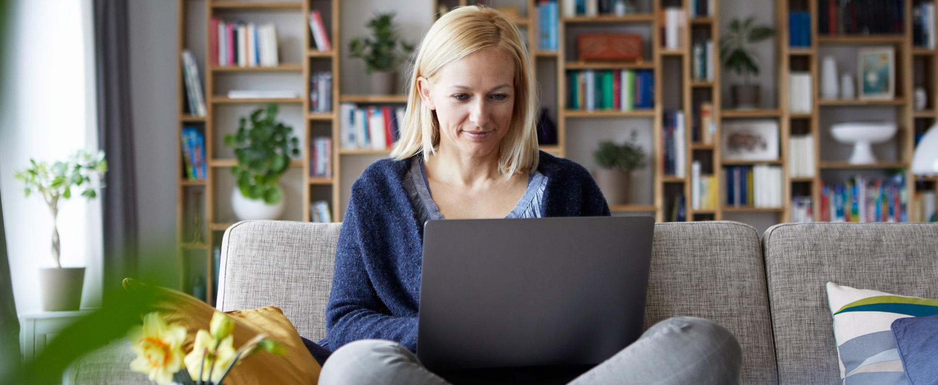 Eine Frau sitzt auf dem Sofa und arbeitet am Notebook. 