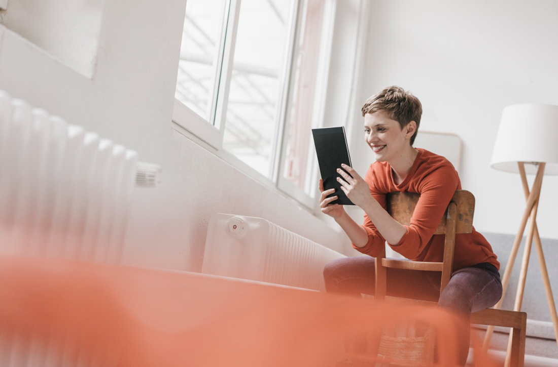 Eine Frau sitzt auf einem Stuhl und schaut auf ihr Tablet.