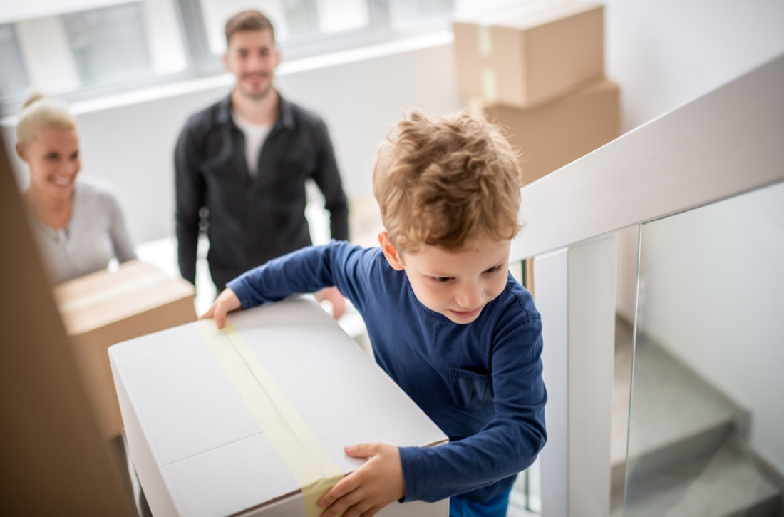 Eltern und ein kleiner Junge tragen Umzugskartons die Treppe hoch. 