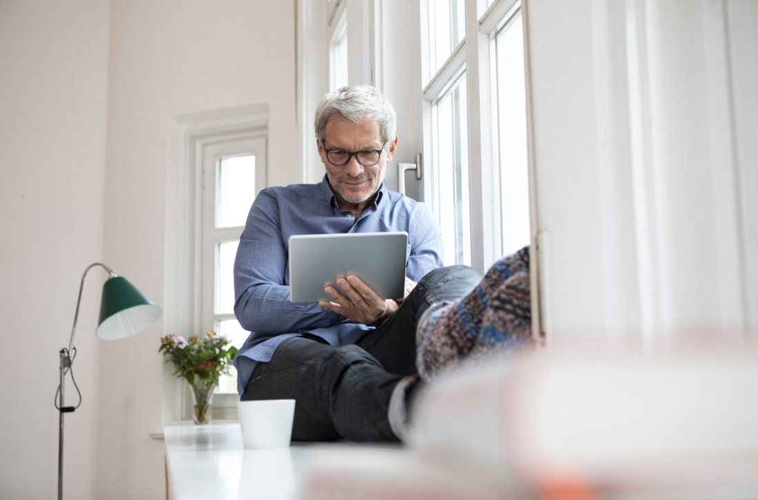 Ein Mann sitzt am Fenster und schaut auf sein Tablet.