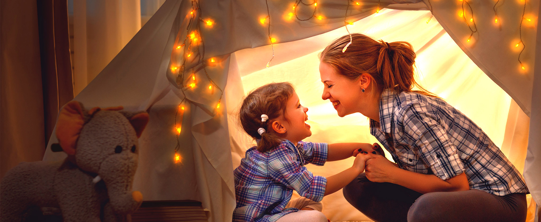Mutter und Tochter sitzen in einem mit einer Lichterkette erleuchteten Zelt in einem Zimmer.