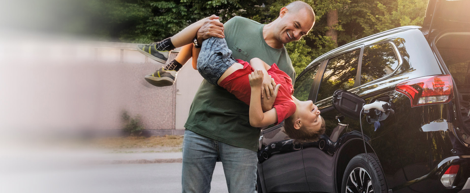 Familie steht zuhause an einem Elektroauto, Vater und Sohn spielen.